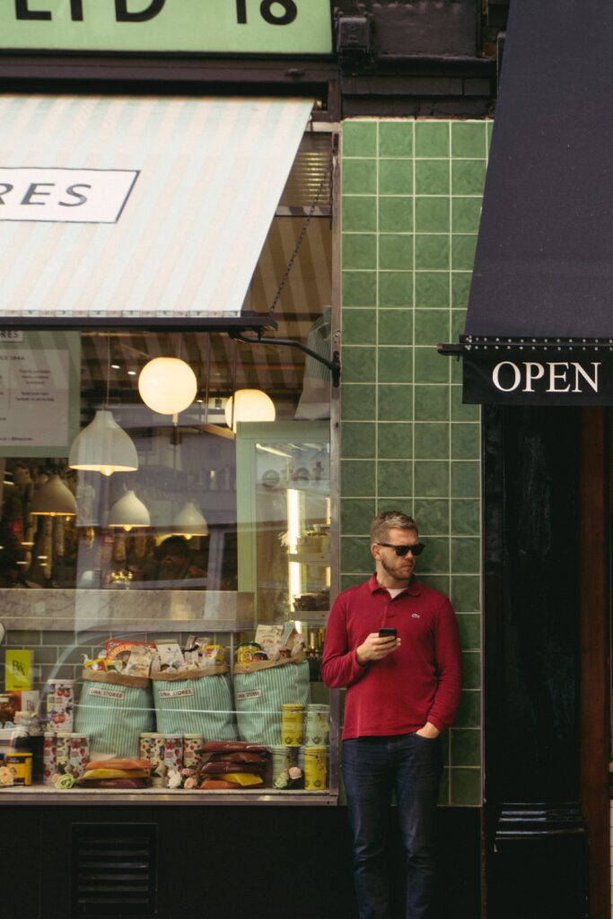 Seorang pria menggunakan smartphone sambil berdiri di luar toko