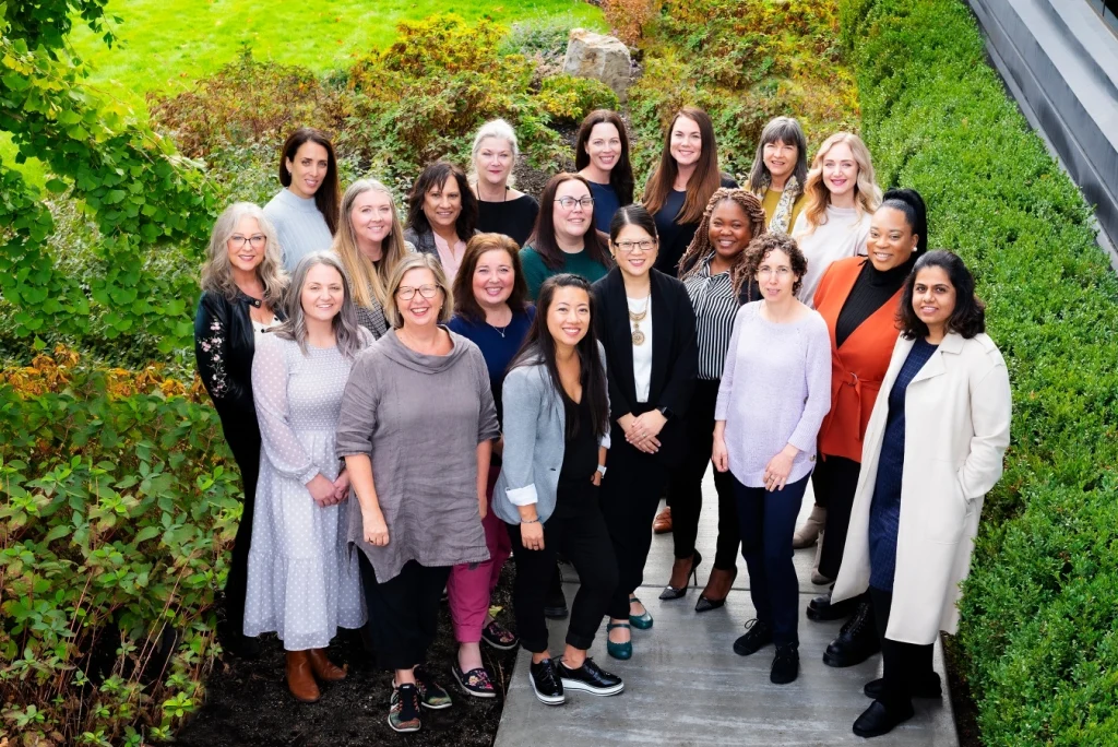 Um grupo de mulheres que trabalham no WeBC se reúne e sorri para uma foto em grupo.