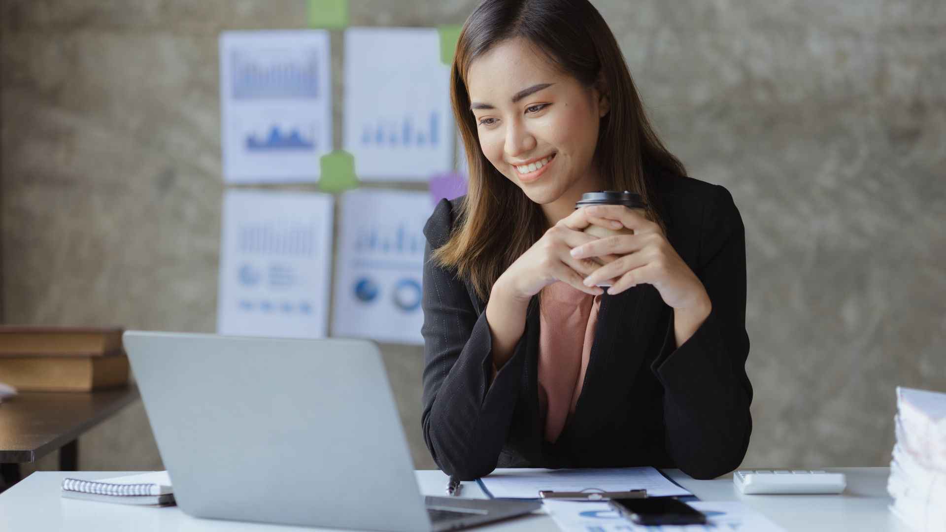 ผู้หญิงคนหนึ่งนั่งข้างจุดหมายปลายทางและดูแล็ปท็อปของเธอด้วยรอยยิ้ม