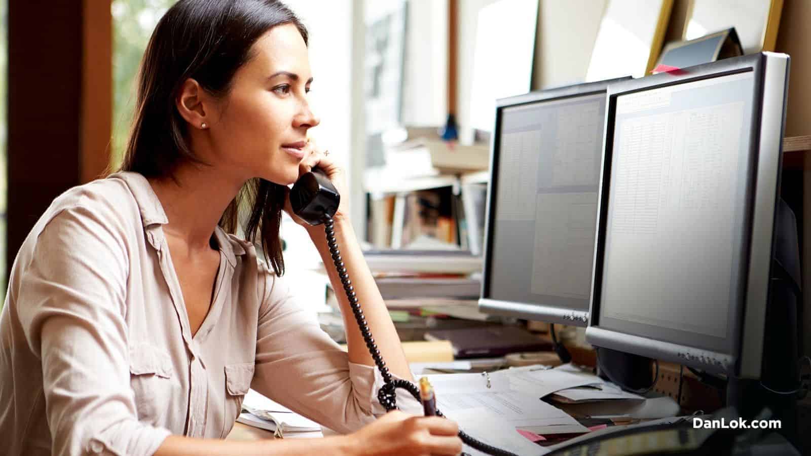Bilgisayarın önünde telefonda konuşan bir kadın, potansiyel olarak telefon üzerinden bir müşteri adayını kapatıyor.